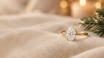 An oval diamond engagement ring in yellow gold on soft ivory fabric, with a subtle evergreen detail